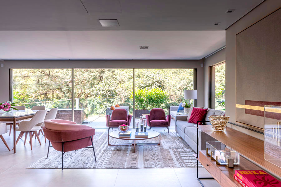 Living amplo com sofás mesa de centro e uma ampla porta de vidro ao fundo que dá acesso a parte externa repleta de verde
